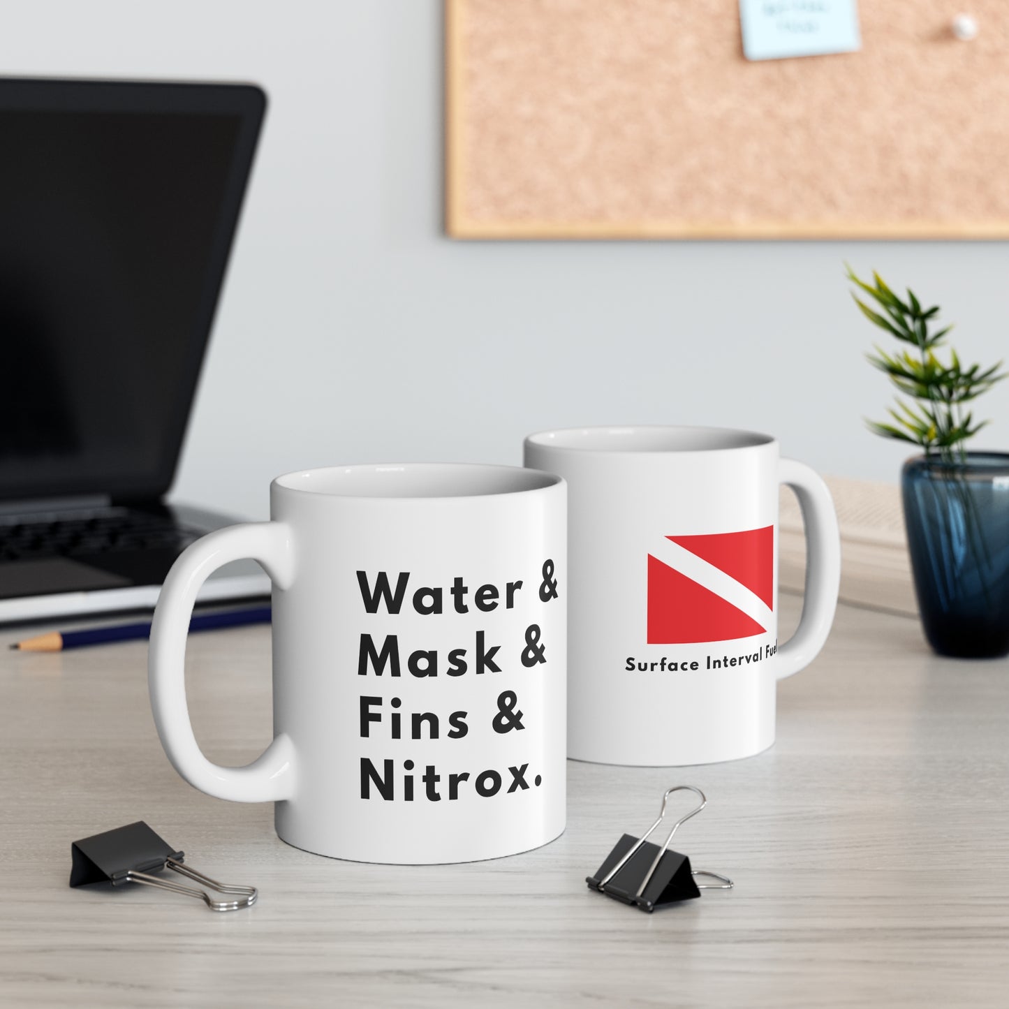 Two mugs on a desk with text and graphics, one featuring a scuba diving flag and the other text about scuba diving equipment such as water, mask, fins, nitrox.