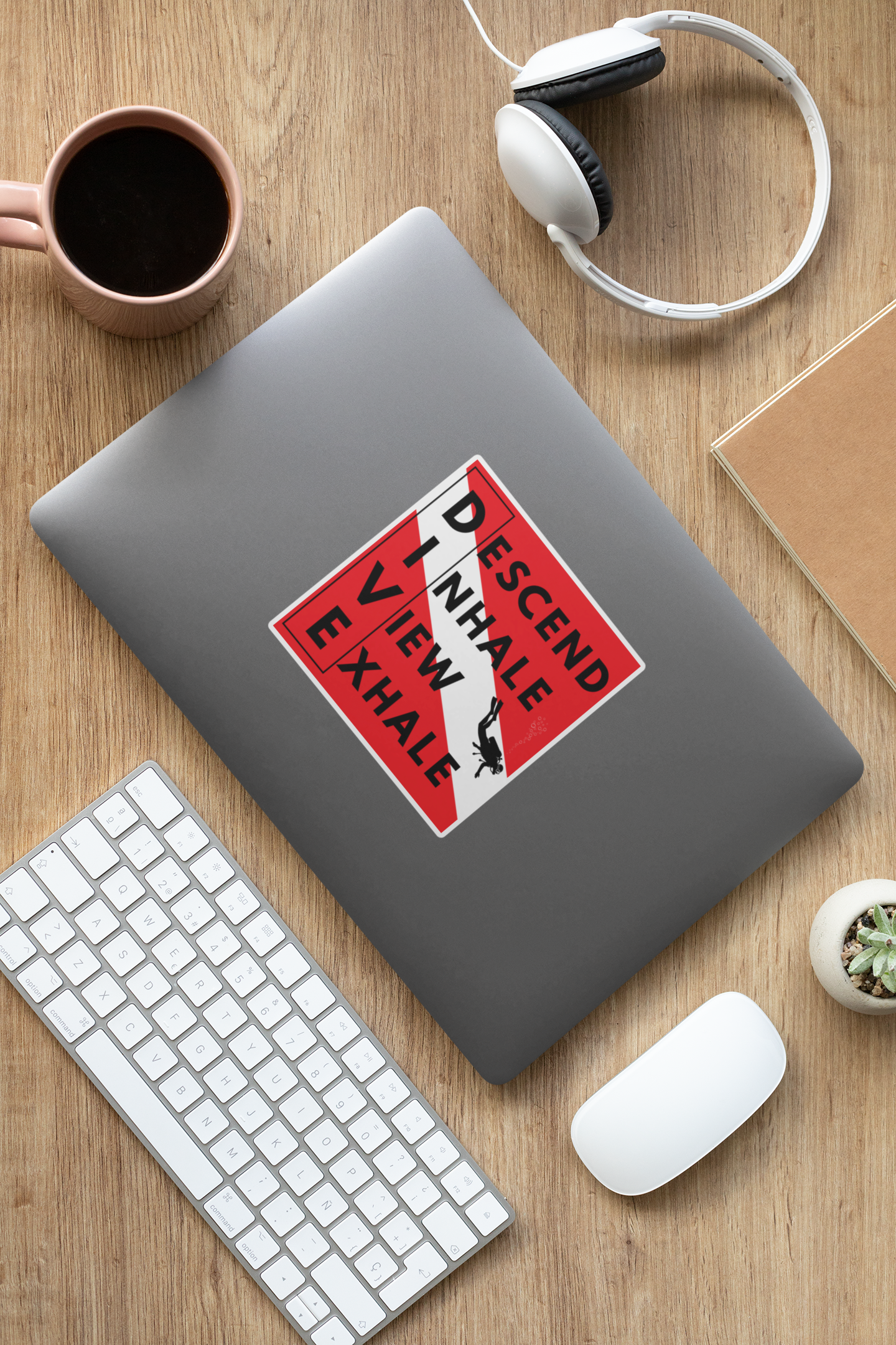 Laptop with a scuba diving sticker on a wooden desk with a keyboard, mouse, and coffee cup.