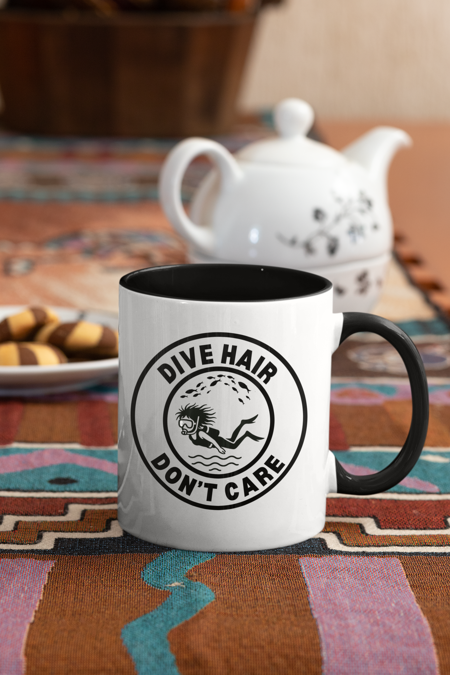 White mug with black handle and 'Dive Hair Don't Care' text on a colorful tablecloth.