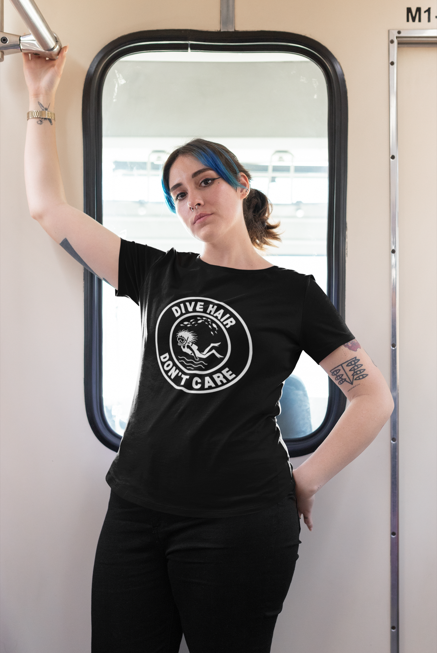 Person wearing a black t-shirt with 'Dive Hair Don't Care' graphic on a train. Scuba Divier.